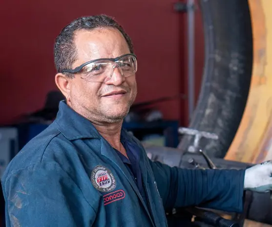 Técnico especialista experimentado sonriendo en un taller, equipado con gafas de seguridad y uniforme de trabajo