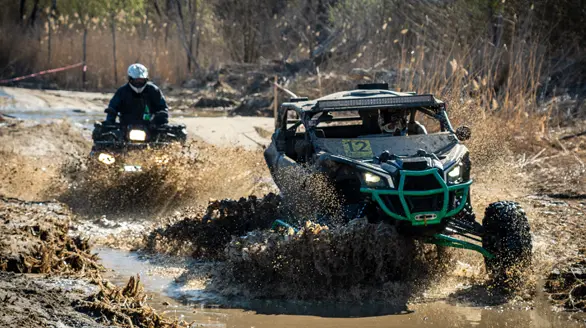 Vehículos todoterreno UTV y ATV atravesando una ruta de lodo y agua a alta velocidad