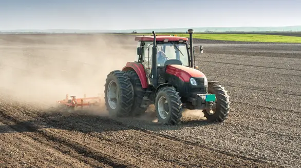 Tractor rojo arando un campo y levantando polvo, representativo del trabajo agrícola pesado
